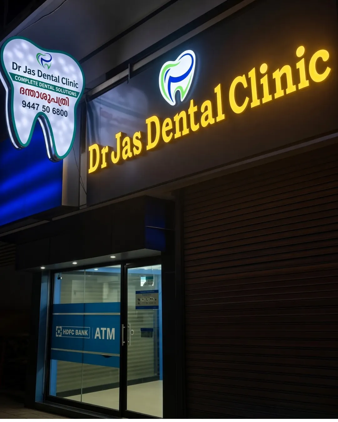 Night-time storefront of Dr Jas Dental Clinic in Pezhakkappilly, next to the HDFC ATM